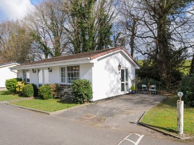 A single story white house with a brown roof and a driveway with two chairs and a table at No 1 The Heathers Rosecraddoc Lodge near Liskeard