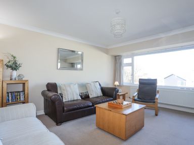 A living room with a brown leather sofa two cushions a wooden coffee table a black armchair and a bookshelf at Tegfan in Trearddur Bay