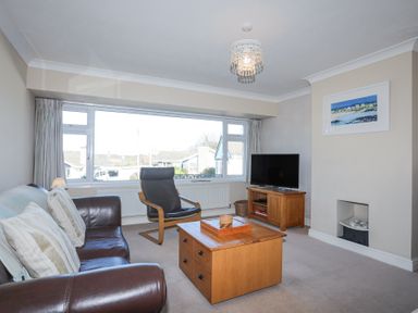 A living room with a brown leather sofa a black armchair a wooden coffee table a television on a stand and a painting on the wall at Tegfan in Trearddur Bay