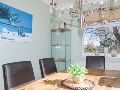 A dining room with a wooden table and black chairs a glass cabinet and a window at Tegfan in Trearddur Bay