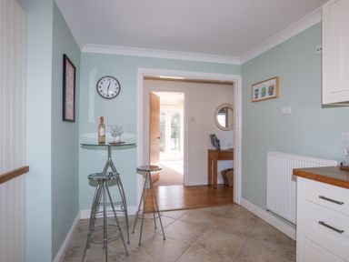A kitchen area with a glass table and stools a bottle of wine and glasses on the table and a clock on the wall at Tegfan in Trearddur Bay