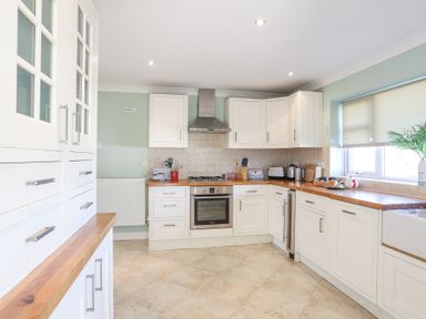 A kitchen with white cabinets wooden countertops a stove and a window with a blind at Tegfan in Trearddur Bay