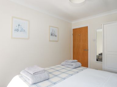 A bedroom with a bed folded towels wooden door white wardrobe and two framed pictures on the wall at Tegfan in Trearddur Bay