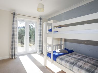 A bedroom with bunk beds next to glass doors with curtains at Tegfan in Trearddur Bay
