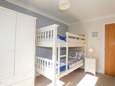 A bedroom with white bunk beds a white wardrobe and a white nightstand with a lamp at Tegfan Trearddur Bay