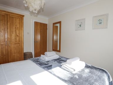A bedroom with a bed folded towels on a gray blanket wooden wardrobe wooden door mirror and two framed pictures on the wall at Tegfan in Trearddur Bay