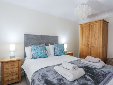 A bedroom with a double bed with blue patterned pillows gray blanket and wooden furniture at Tegfan in Trearddur Bay