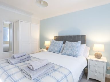 A bedroom with a double bed two bedside tables with lamps a wardrobe and a full length mirror at Tegfan in Trearddur Bay