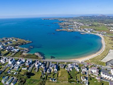 A coastal area with houses along a curved beach and a bay at Tegfan in Trearddur Bay