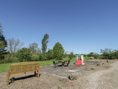 An outdoor area with a wooden bench a picnic table with chairs and a children's slide in a field at Goathland Cottage Ruswarp near Whitby