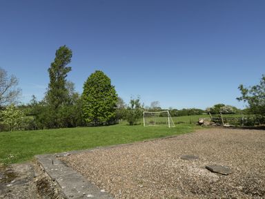 A grassy field with a soccer goal and gravel area bordered by trees at Goathland Cottage in Ruswarp near Whitby