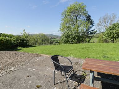An outdoor patio area with a black chair and wooden picnic table overlooking a grassy field with trees at Goathland Cottage in Ruswarp near Whitby