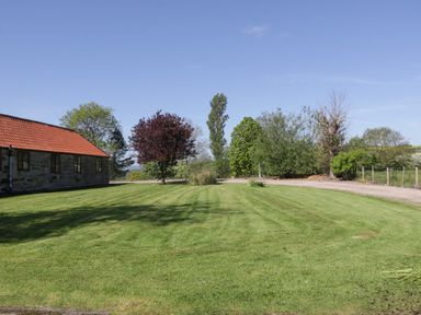A lawn with trees and a stone building with a red-tiled roof at Goathland Cottage Ruswarp near Whitby