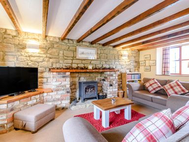 A living room with wooden beams on the ceiling a stone fireplace a television couches with plaid pillows and a wooden coffee table on a red rug at Goathland Cottage Ruswarp near Whitby