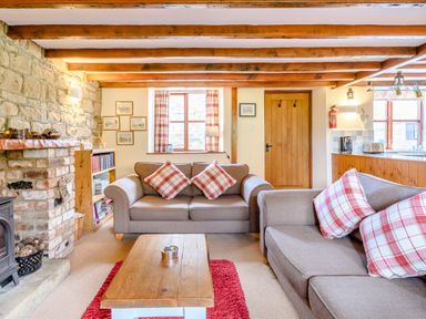 A living room with two sofas, a wooden coffee table, a stone fireplace, and exposed ceiling beams at Goathland Cottage in Ruswarp near Whitby