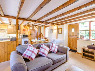 An open plan living area with a sofa with three checked cushions a wooden dining table with set places a kitchen area a wooden staircase and a wooden door at Goathland Cottage Ruswarp near Whitby