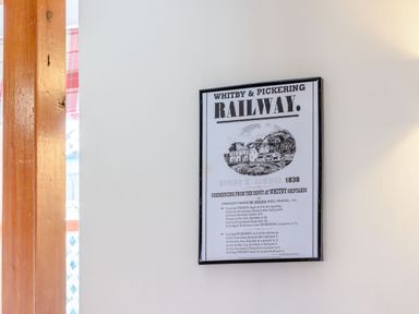 A framed poster about Whitby and Pickering Railway on a white wall with part of a wooden post and red check curtain visible at Goathland Cottage Ruswarp near Whitby