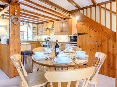 A kitchen with wooden cabinets a dining table set with plates bowls and wine glasses and wooden chairs at Goathland Cottage in Ruswarp near Whitby