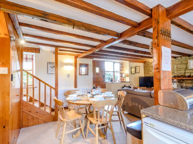 A dining area with a wooden table and chairs set with dishes and glasses next to a living room with a television and sofa at Goathland Cottage in Ruswarp near Whitby