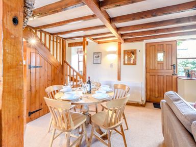 A dining area with a wooden table set for six and wooden chairs near a wooden staircase and door at Goathland Cottage in Ruswarp near Whitby