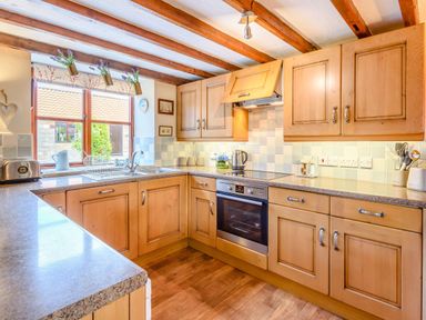 A kitchen with wooden cabinets a countertop an oven a window with potted plants and wooden beams on the ceiling at Goathland Cottage in Ruswarp near Whitby