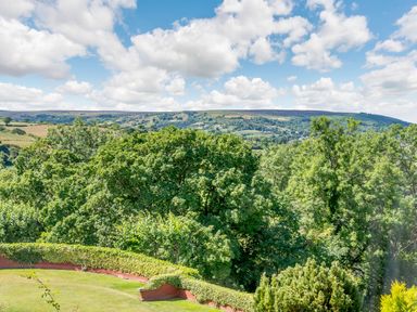A garden with grass hedge and trees overlooking hills under a partly cloudy sky at Goathland Cottage Ruswarp near Whitby
