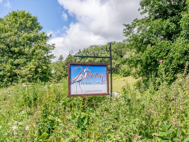 A sign for Heron Holiday Cottages at Lambert Hill Farm surrounded by greenery and trees