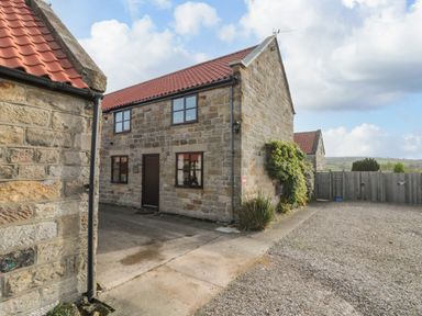 A stone house with a red tiled roof next to a gravel driveway and wooden fence at Goathland Cottage in Ruswarp near Whitby