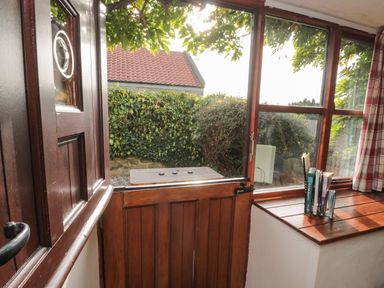 A wooden stable door open to a garden with hedge and bushes seen through window at Goathland Cottage Ruswarp near Whitby