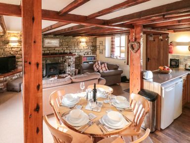 A dining table set for six in an open living area with exposed wooden beams and a stone fireplace at Goathland Cottage Ruswarp near Whitby