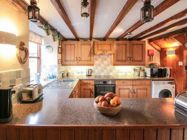 A kitchen with wooden cabinets a countertop bowl of fruit and appliances at Goathland Cottage in Ruswarp near Whitby