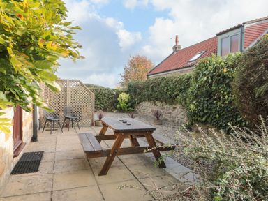 An outdoor patio area with a wooden picnic table and two black chairs at Goathland Cottage in Ruswarp near Whitby