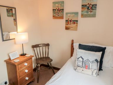 A bedroom corner with a wooden chair beside a nightstand with a lamp and a bed with decorative pillows at Goathland Cottage in Ruswarp near Whitby