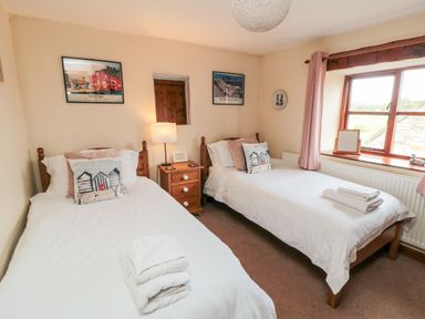 A bedroom with two single beds a wooden nightstand with a lamp and window with pink curtains at Goathland Cottage Ruswarp near Whitby