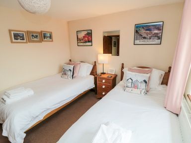A bedroom with two single beds a wooden nightstand with a lamp and framed pictures on the walls at Goathland Cottage in Ruswarp near Whitby