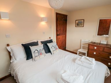 A bedroom with a bed with pillows and folded towels wooden door wooden dresser with mirror and chair at Goathland Cottage in Ruswarp near Whitby