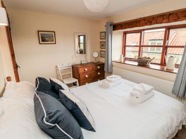 A bedroom with a bed white towels on the bed a wooden dresser a white chair and a window overlooking rooftops at Goathland Cottage Ruswarp near Whitby