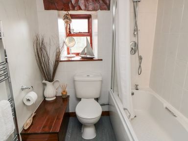 A bathroom with a toilet next to a bathtub and a wooden bench holding a vase with sticks and a reed diffuser at Goathland Cottage Ruswarp near Whitby
