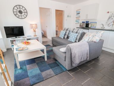 A living room with a gray sofa and pillows beside a white coffee table and a television at Bracken Barn Cottage Widdrington near Amble