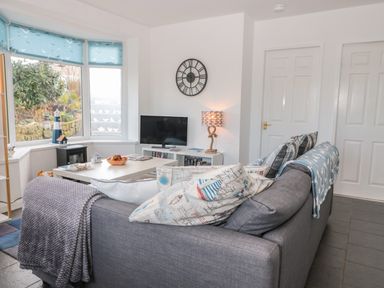 A living room with a gray sofa and patterned cushions a white coffee table and a television on a stand at Bracken Barn Cottage in Widdrington near Amble
