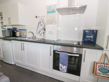 A kitchen with white cabinets a black countertop a stainless steel oven a microwave kettle and a bread bin at Bracken Barn Cottage in Widdrington near Amble