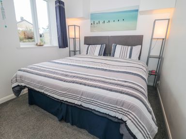A bedroom with a double bed, striped bedding, two floor lamps, a window with curtains, and a wall picture at Bracken Barn Cottage in Widdrington near Amble