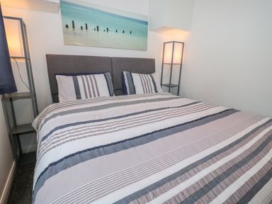A bedroom with a double bed with striped bedding two bedside shelves two lamps and a beach photograph on the wall at Bracken Barn Cottage in Widdrington near Amble