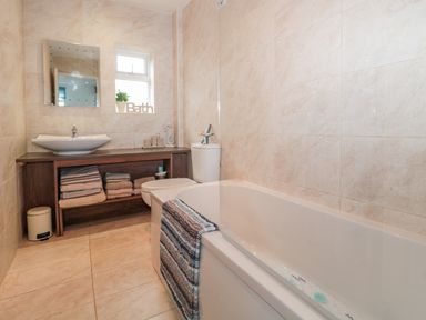 A bathroom with a bathtub a sink a toilet towels and a small window at Bracken Barn Cottage Widdrington near Amble