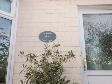 An exterior wall with a sign reading Bracken Barn Cottage next to a door with frosted glass and a plant in front of the wall at Bracken Barn Cottage Widdrington near Amble