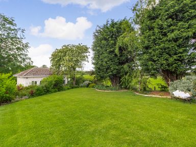 A green lawn with trees shrubs a bench and a white building at Bracken Barn Cottage in Widdrington near Amble
