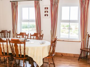 A dining room with a wooden table and chairs near two windows with striped curtains at McGuire's Cottage in Barnatra County Mayo