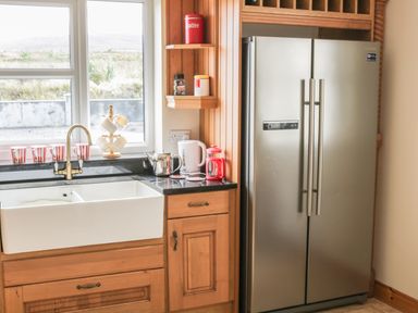 A kitchen sink with cups on the windowsill a kettle a French press a coffee canister wooden cabinets and a stainless steel refrigerator at McGuire's Cottage in Barnatra County Mayo