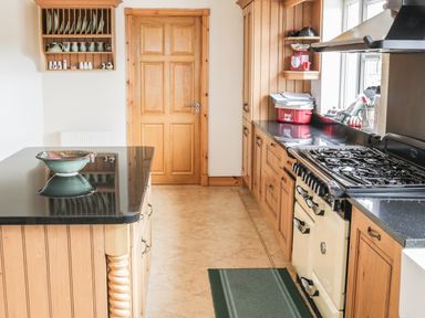 A kitchen with wooden cabinets a stove a countertop with a bowl and a door at McGuire's Cottage Barnatra County Mayo