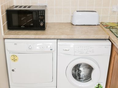 A kitchen counter with a black microwave and white toaster on top and a white dryer and washing machine below at McGuire's Cottage Barnatra County Mayo